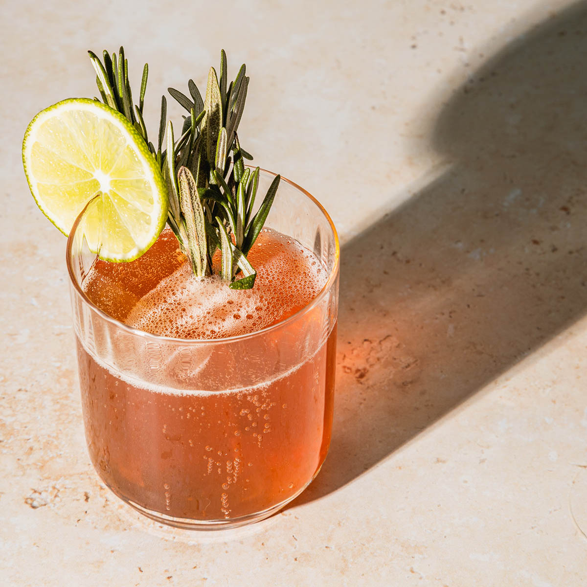 Cocktail glass with lime and garnish on stone table.